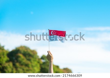 hand holding Singapore flag on blue sky background. Singapore National Day and happy celebration concepts