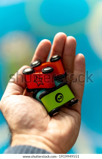 A hand holding small flat colorful toy cars with\
numbers on them