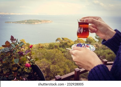 Hand Holding Small Glass Of Turkish Tea In Front Of The Sea. Toned Image