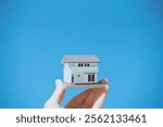 Hand holding a small house, blue sky background