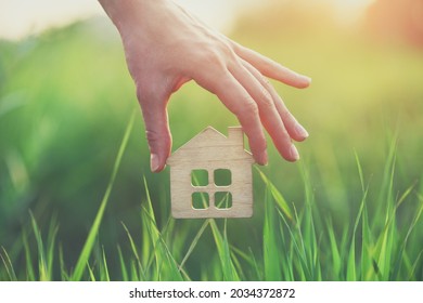Hand holding small wooden house in green grass, safe, sweet and eco accommodation concept, shelter, home loan and insurance, family life 