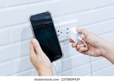 Hand holding smart phone and adaptor to connect to power outlet wall, Hand pluging adapter with outlet socket plug and hold mobile.
