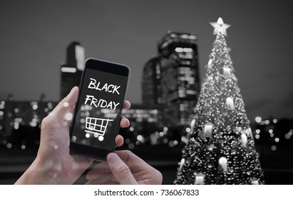 Hand Holding Smart Phone, Black Friday And Shopping Cart, Abstract Blurred Black And White Festive Light Bokeh On Christmas Tree Decoration On Black Background, Black Friday Holiday Shopping Concept