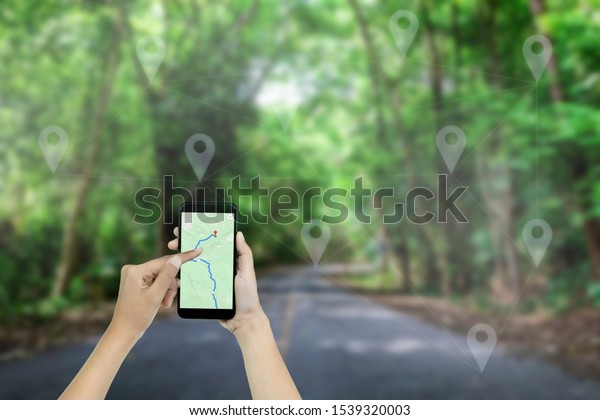 Hand holding a smart phone of map navigator on\
connection on the road in\
forest.