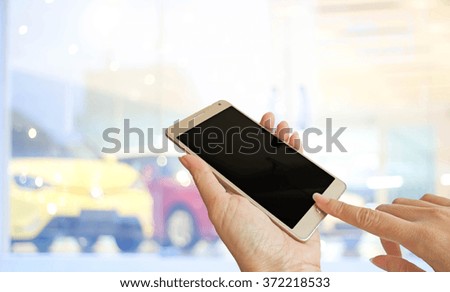hand holding smart phone on background blurred photo of car showroom