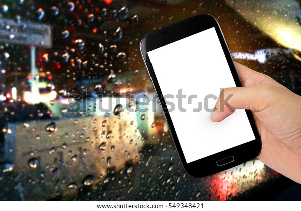 Hand holding smart phone with raining drops on\
the car window.