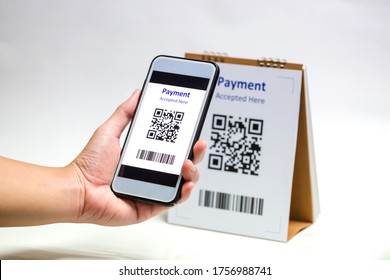 Hand Holding Smart Phone To Scan QR Code Payment On White Background. The Concept Of Cashless Technology Or Digital Payment.