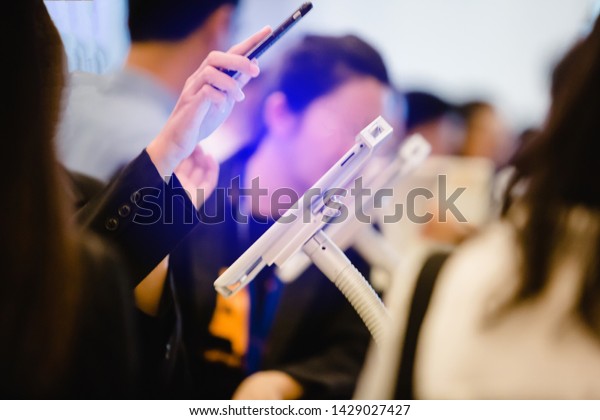 hand\
holding smart phone and scan QR code over tablet for registration\
in to seminar or meeting with blurry people background. selective\
focus. the concept of electronic\
registration.