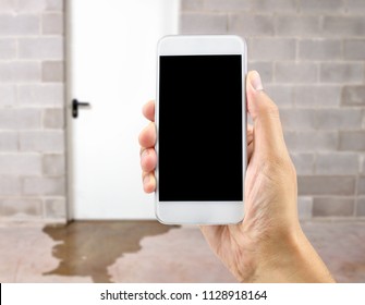 A hand holding up a smart phone with water damage in basement caused by sewer backflow due to clogged sanitary drain background 