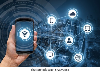 Hand holding smart phone, wireless communication network on city background