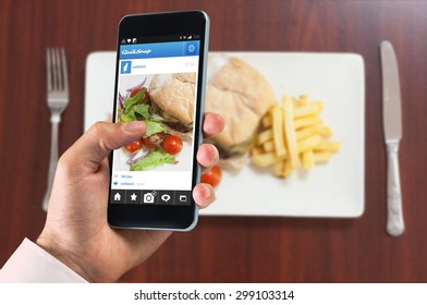 Hand Holding Smartphone Against Overhead View Of Burger With French Fries And Salad