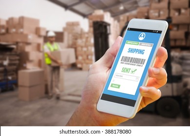 Hand holding smartphone against warehouse worker loading up pallet