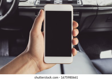 A hand holding a smartphone with a blank screen in the car