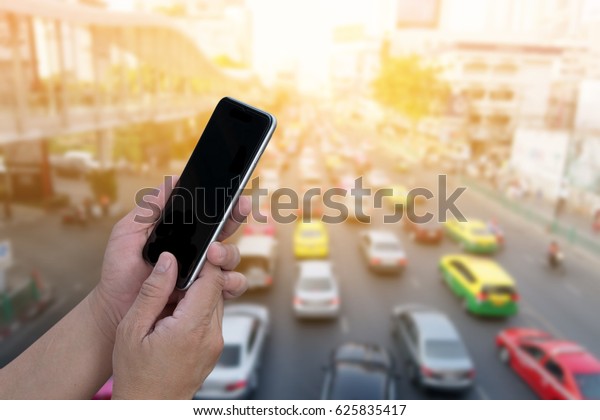 hand holding smartphone with blurred traffic jam\
background for concept internet of things; smart life; digital\
online; traffic report.