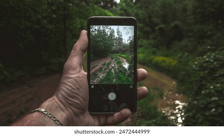 Hand holding smartphone capturing a muddy trail in a lush green forest. - Powered by Shutterstock