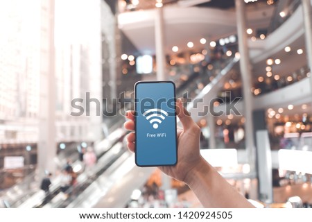 Hand holding smartphone with free wifi icon on blurred shopping mall background.