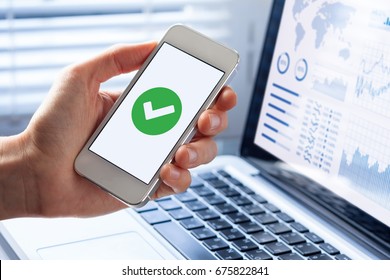 Hand holding a smartphone with a green checkmark icon on the screen to show a validated, confirmed, completed or approved status - Powered by Shutterstock