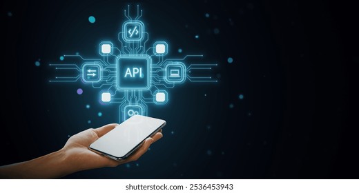 A hand holding a smartphone with holographic API icons connecting to technology symbols on a dark blue abstract background. Represents online data integration and modern business software concept