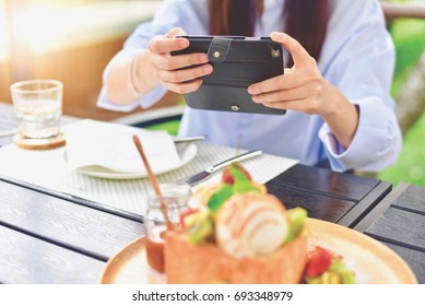 Hand Holding a Smartphone While Taking a Photo of Desserts