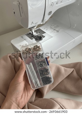 Hand Holding Snap Button Tool Kit in Front of a Sewing Machine