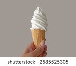 Hand holding Soft Serve Vanilla Ice Cream Cone isolated on plain beige background.