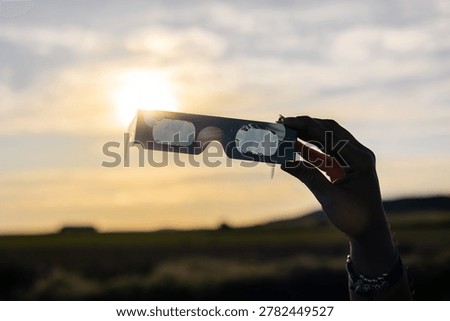 Hand holding solar eclipse glasses viewing a partial solar eclipse during sunset, safe observation of celestial event