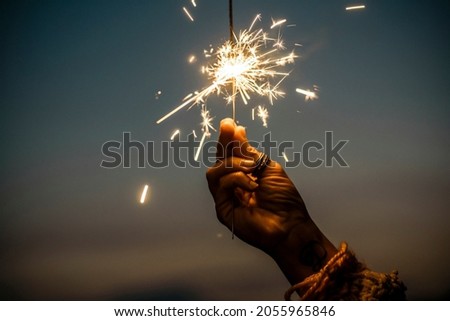 Hand holding sparkler firework firing with sunset sky in background - concept of new year eve celebration people - hope and love image of woman dreams - warm tones
