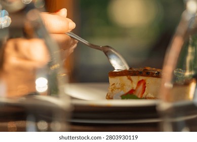 Hand holding a spoon, scooping a bite of delicious cheesecake topped with vibrant passion fruit glaze and a fresh strawberry slice, enjoying a sweet dessert