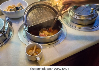 Hand Holding Spoon Of Sour Soup From Stainless Container In Salad Bar Area.