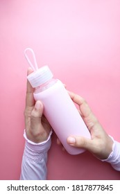 hand holding sport bottle isolated on pink, top view .