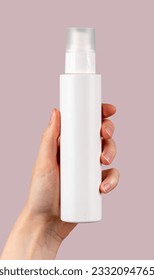 Hand holding spray bottle mockup, blank beauty product on pink background.