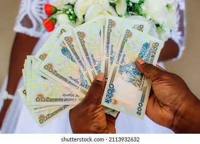 Hand Holding Spread Of Multiple Nigerian Naira Notes, Cash, Currency Or Money With A Bride And Bouquet At The Background Of The Shot