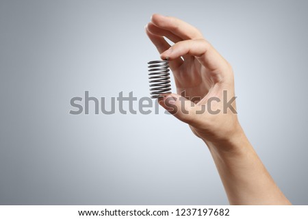 Hand holding a spring on grey background