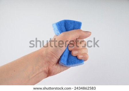 A hand (holding) squeezes blue washing sponge for dishes isolated on a white background