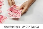 Hand Holding Stack of 100 Yuan Notes on table.  Translate alphabet Yibai yuan meaning one hundred yuan.