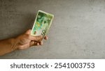 Hand holding a stack of israeli shekel banknotes against a concrete background