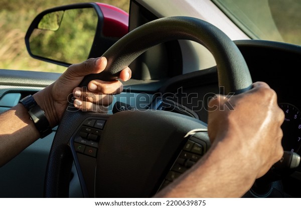 The hand is holding the steering wheel of the car\
Safe driving. Close-up Of A Man Hands Holding Steering Wheel While\
Driving Car