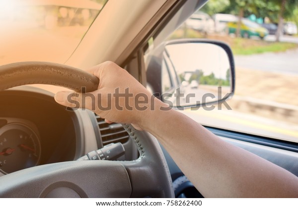 The hand holding the\
steering wheel to control the car. Control the car inside the\
cabin. Driving the car and looking at the side mirror. Close\
up.\
Selective focus.\
flare.