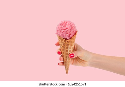Hand holding strawberry ice cream cone on pink faded pastel color background. Strawberry ice cream in wafer cup.