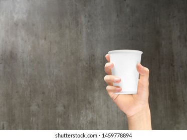 Hand Holding A Styrofoam Cup With Coffee On The Wooden Wall Background