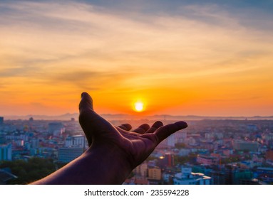 Hand holding sunset and city of background. - Powered by Shutterstock