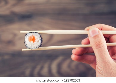 Hand holding sushi roll using chopsticks on wooden background