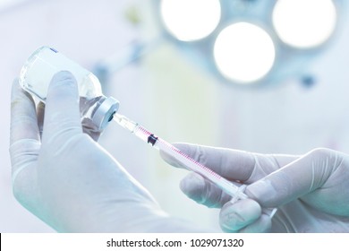 Hand holding syringe and medicine vial prepare for injection in operating room with surgery lamp background - Powered by Shutterstock