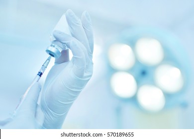 Hand holding syringe and medicine vial prepare for injection in operating room with surgery lamp background. - Powered by Shutterstock