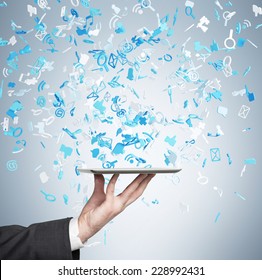 A hand holding a tablet with flying social networking icons. Blue background.  - Shutterstock ID 228992431