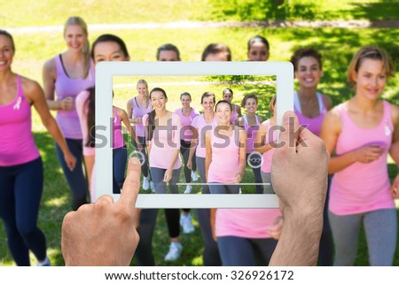 Hand holding tablet pc against smiling women in pink for breast cancer awareness