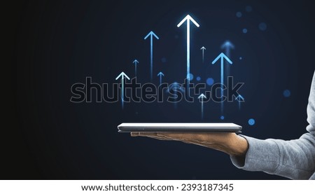 Hand holding tablet with rising arrows hologram, depicting growth and digital progress concept