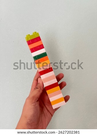 A hand is holding a tall vertical stack of colorful interlocking plastic blocks (similar to LEGO).