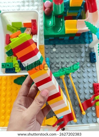 A hand is holding a tall vertical stack of colorful interlocking plastic blocks (similar to LEGO).