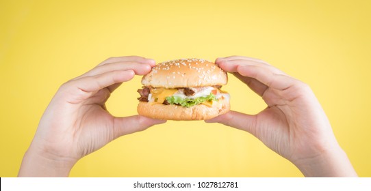 Hand holding tasty hamburger against yellow background,Close up